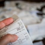 Persona anziana che consulta un elenco di spese, riflettendo su cambiamenti finanziari.