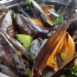 Cozze alla tarantina servite in un piatto con pomodoro e prezzemolo fresco.